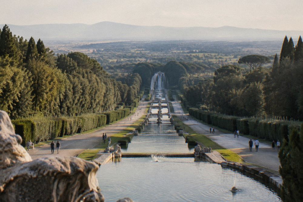 A long garden cascade with fountains and statues running uphill away from a palace