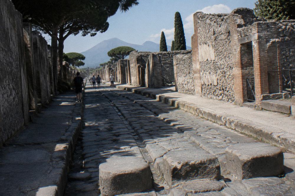 Stone-paved ancient street with cart ruts and ruined walls under a clear sky