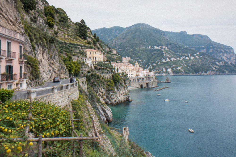 Cliffside houses above a narrow coastal road curving around a turquoise bay
