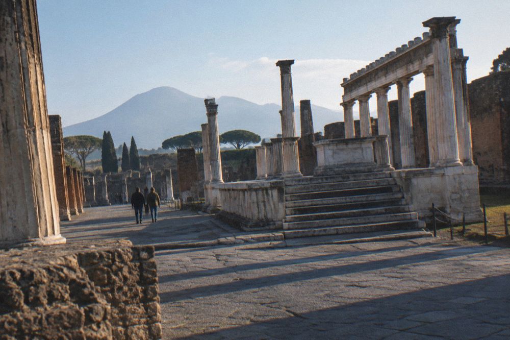 Wide excavated Roman square with column stumps and Mount Vesuvius rising behind