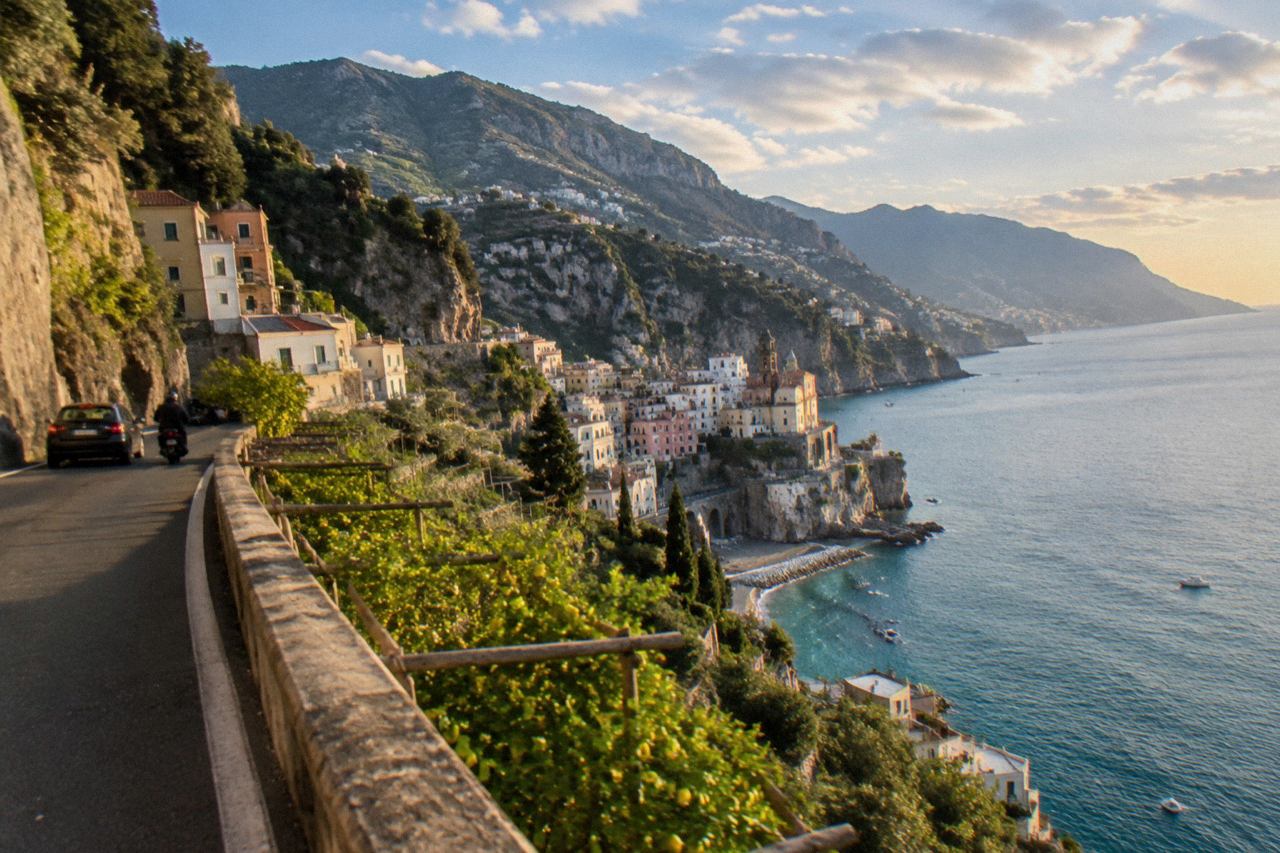 Cliffside houses above a narrow coastal road curving around a turquoise bay