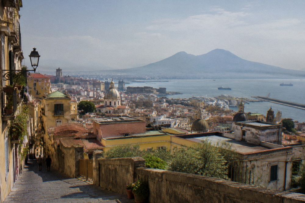A road winding down a hillside toward rooftops and a distant bay