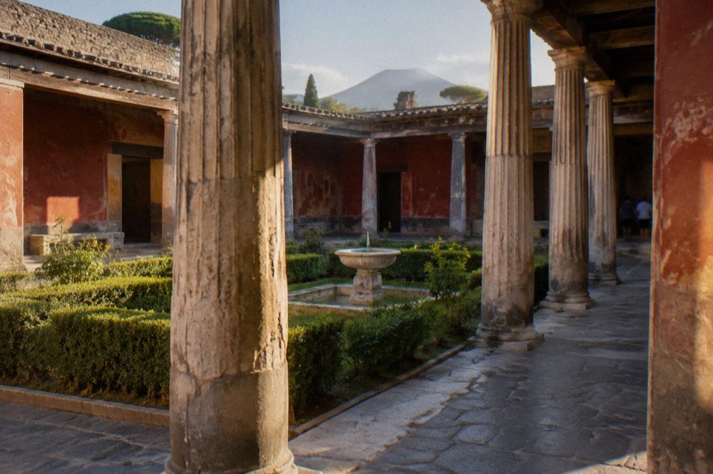 A rural railway platform with the ancient walls of Pompeii rising behind it under a clear sky