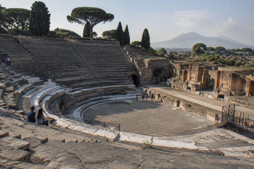 Wide view over Pompeian roofless houses toward distant mountains at golden hour