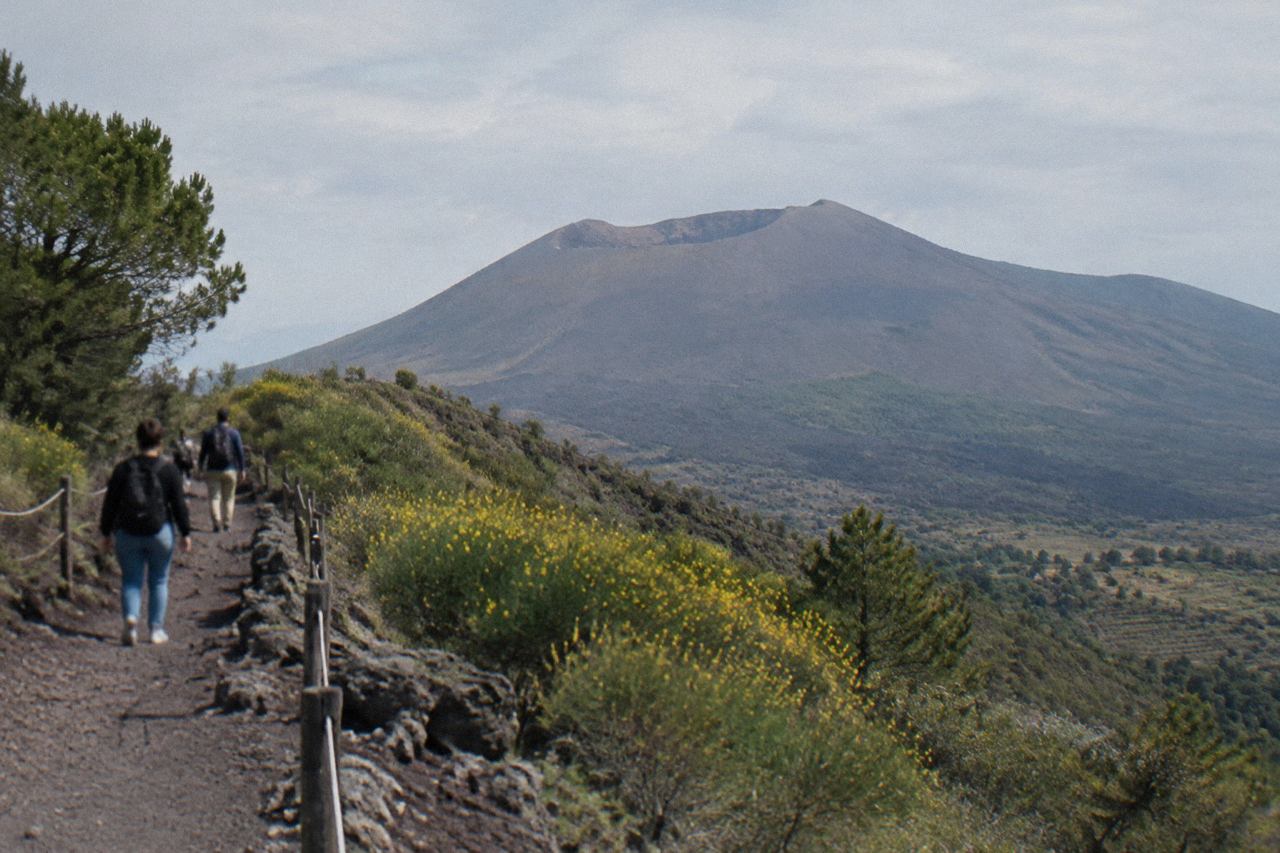 The Gran Cono crater rim of Mount Vesuvius under a clear sky, with the Bay of Naples in the distance