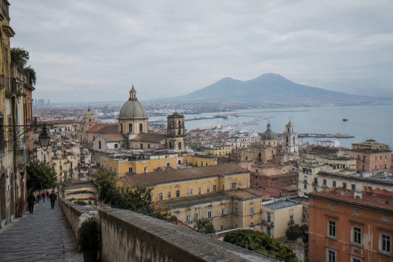The stone street and ruined walls of Pompeii under a wide sky with Vesuvius on the horizon
