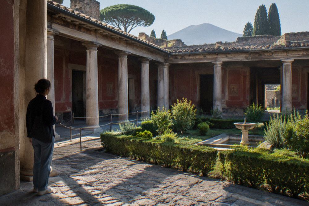 A wide ancient stone-paved street in Pompeii lined with ruined walls under a bright sky