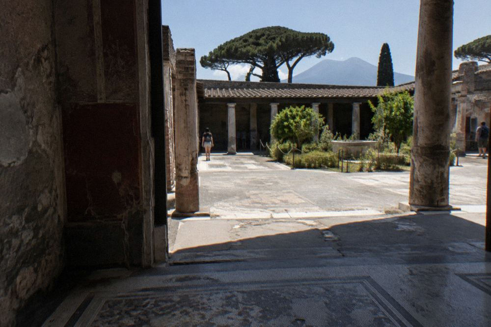 Wide view across Pompeii ruins with Mount Vesuvius rising in the background under a blue sky