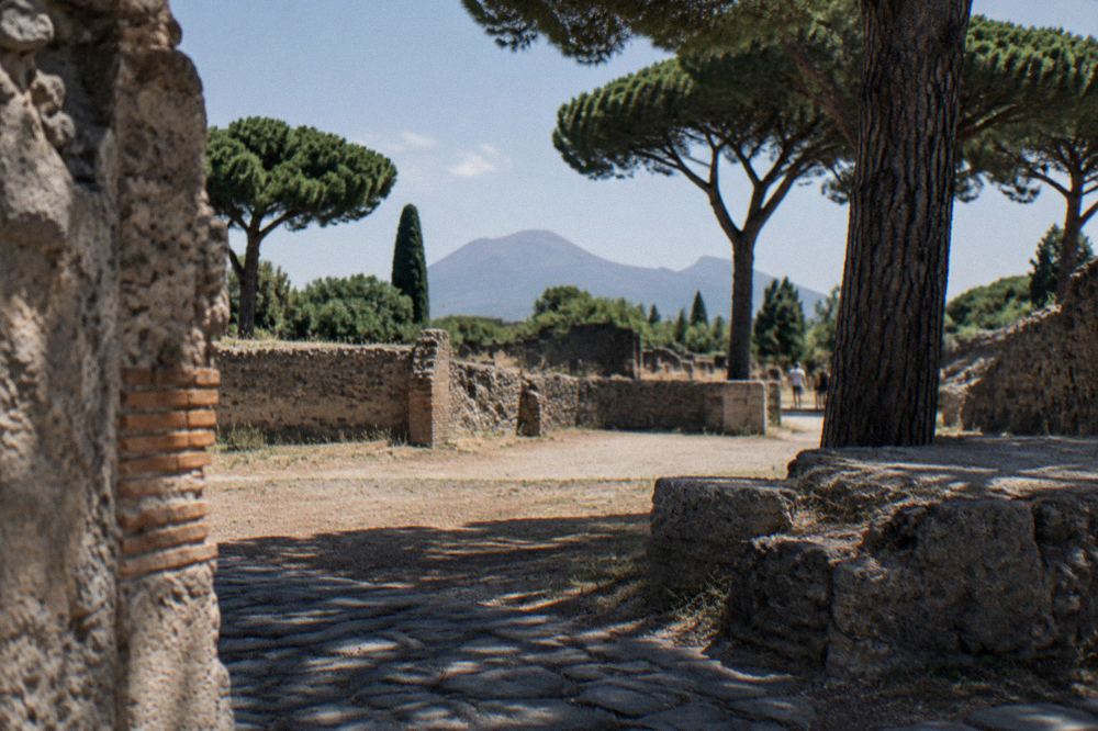 Visitors walking an ancient stone-paved street of Pompeii lined with ruined walls