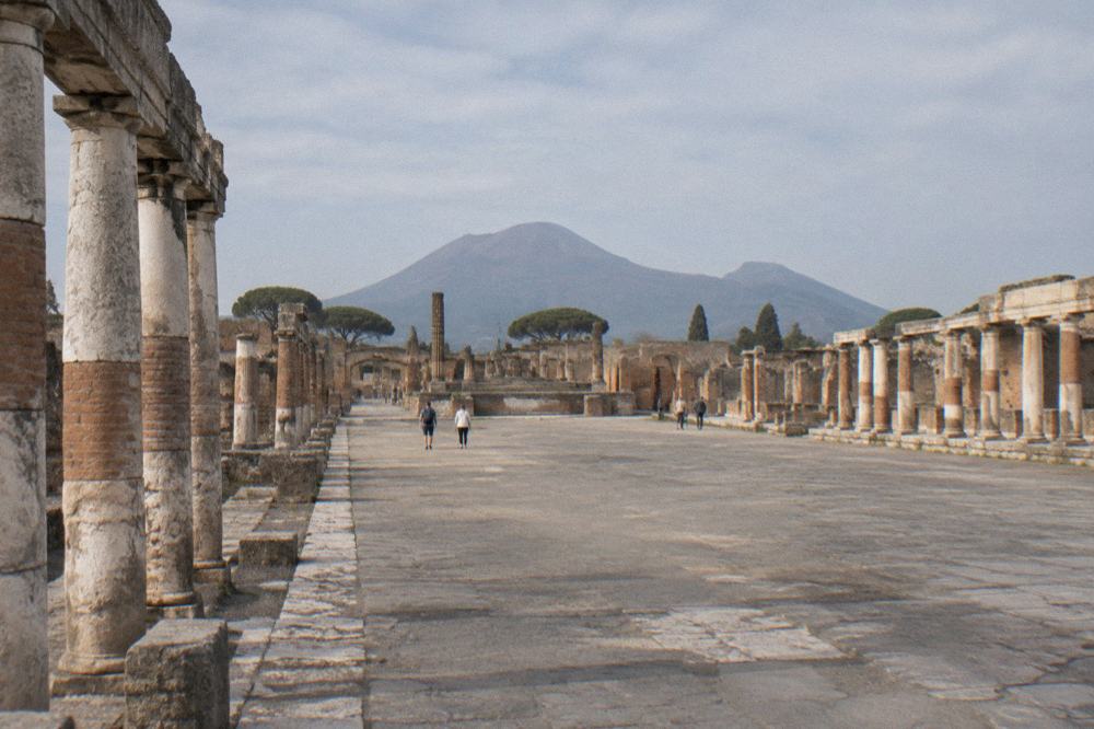 A line of ancient Roman columns along a ruined street with Vesuvius rising in the background