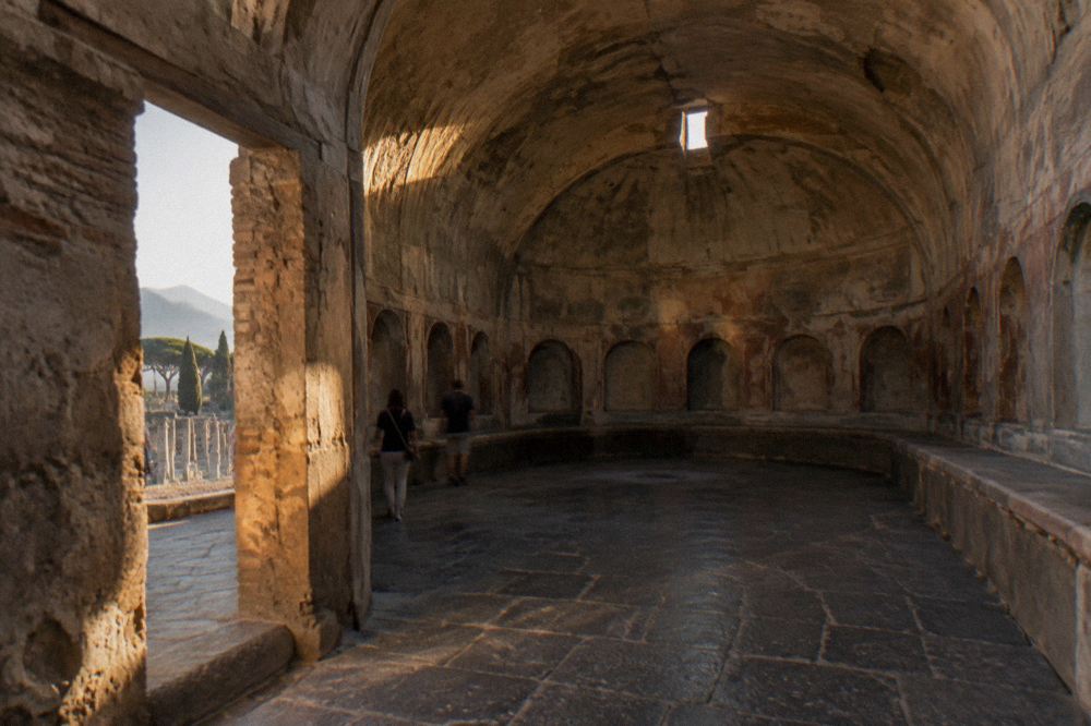Wide view across the ruins of Pompeii with stone streets and Mount Vesuvius on the horizon