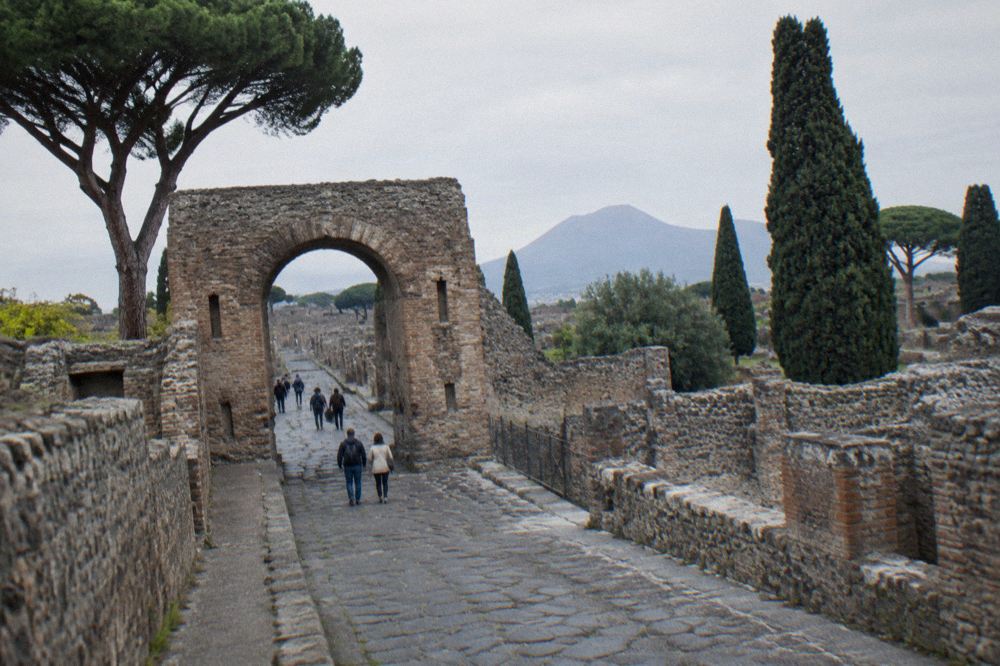 Queue of visitors waiting at a stone entrance gate of Pompeii in warm morning light