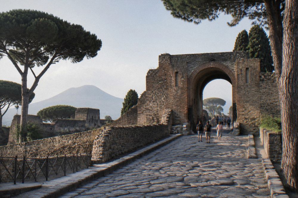 Guide book lying open on a wooden bench with the dark excavated ruins of Herculaneum behind it under a clear sky