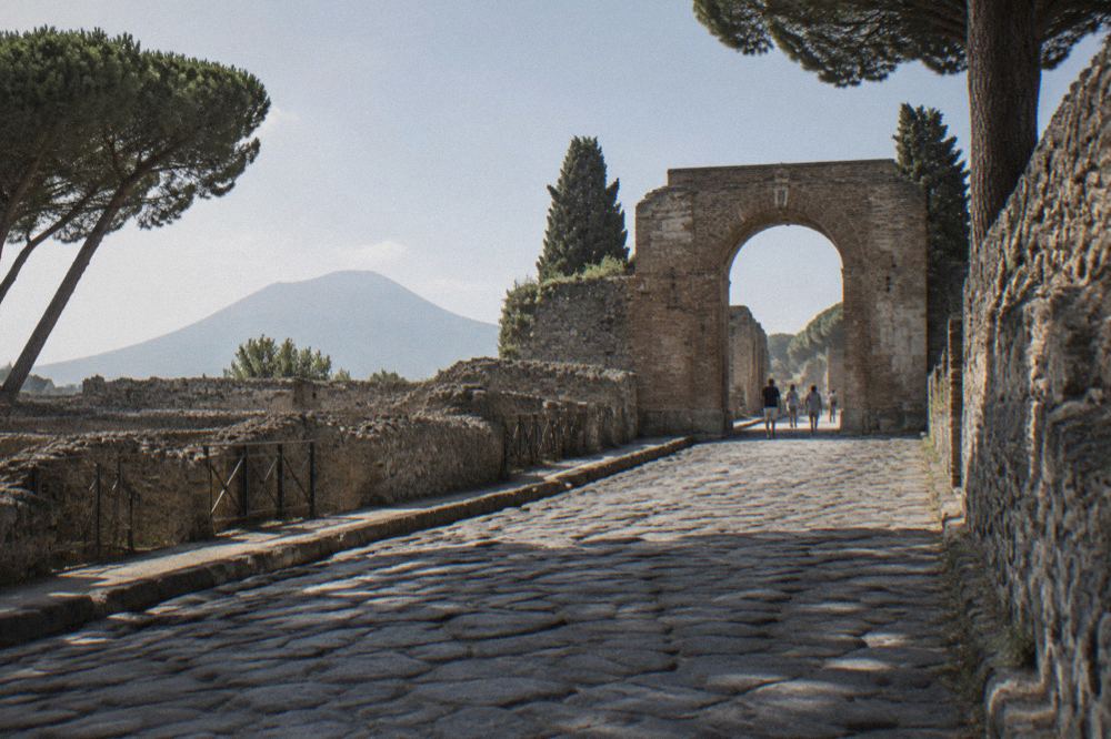 Ancient Roman street of stone paving stretching toward a stone arch under a strong midday sun with few shadows
