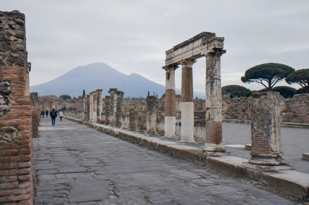 Crowded ancient colonnaded square in Pompeii seen from a raised walkway