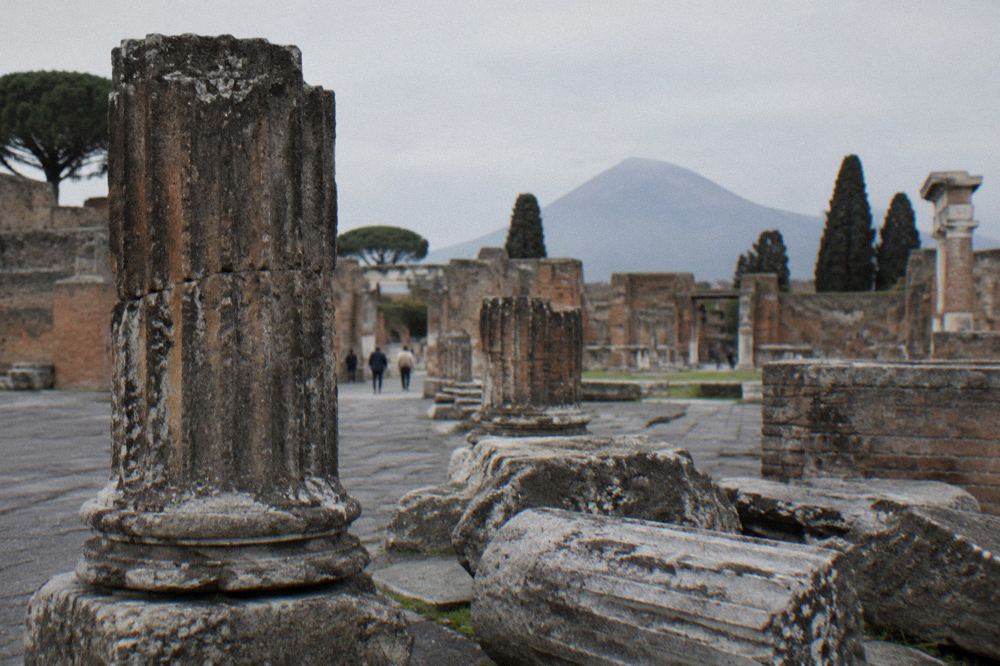 Visitors with backpacks entering an arched stone gateway at Pompeii