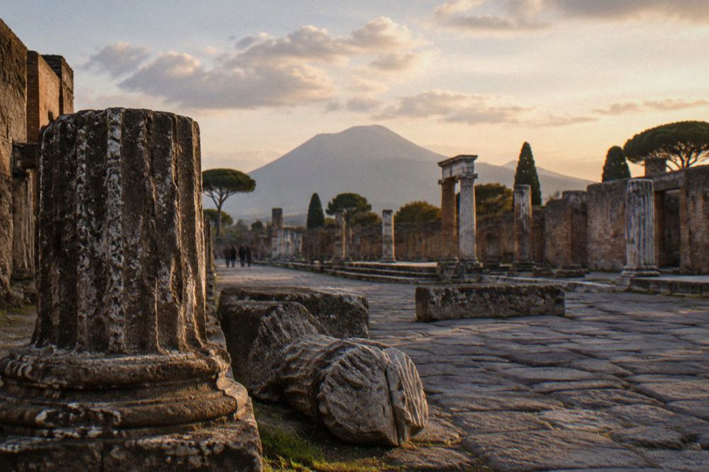 The stone street and ruts of Pompeii under low evening light with Vesuvius on the horizon