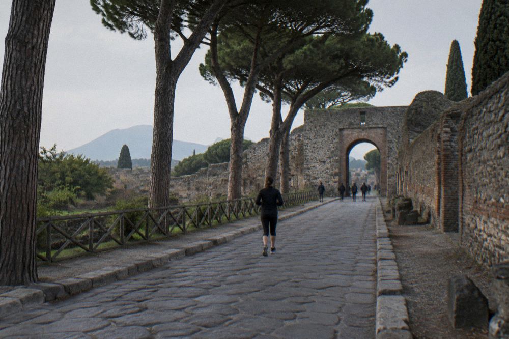A wide view across the excavated ruins of Pompeii toward Mount Vesuvius under a blue sky