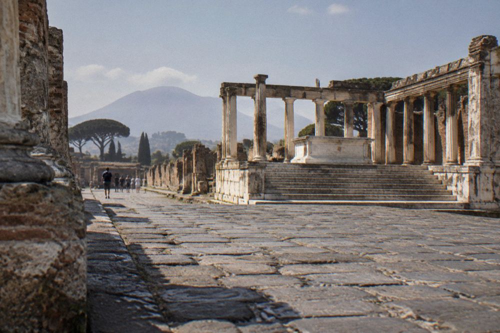 Worn basalt paving of a Pompeii street showing deep cart ruts and raised crossing stones under strong sun