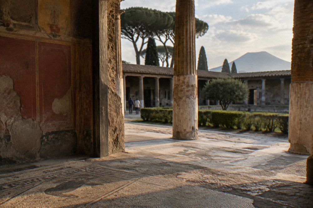 Long straight ancient street in Pompeii under strong midday sun with high stone walls and little shade
