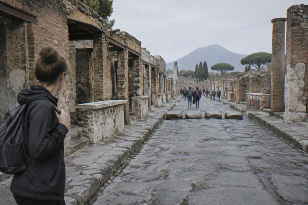 A single-track rural railway curving past orange groves and residential buildings toward a distant volcano cone