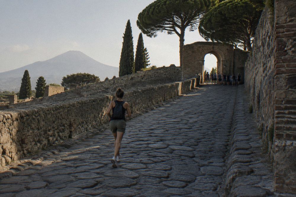 Ancient stone-paved streets of an excavated Roman city under a warm afternoon sky with Vesuvius on the horizon