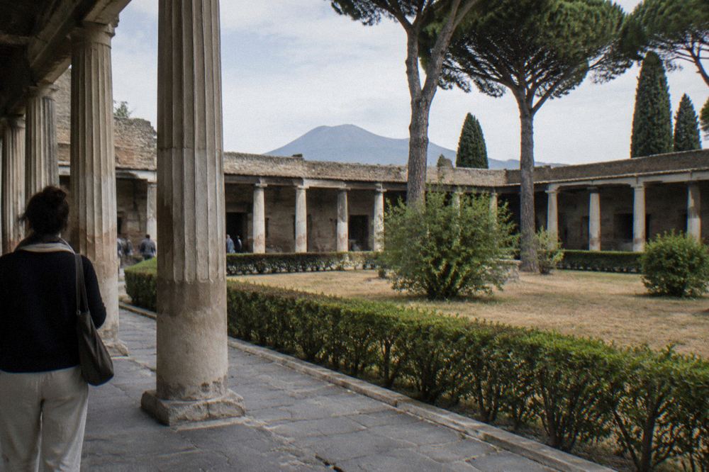 Visitors walking on the ancient basalt paving stones of Pompeii under a bright summer sun with Mount Vesuvius in the background