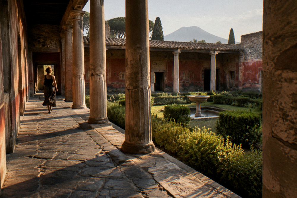 Wide view over the excavated ruins of Pompeii toward the sea in soft evening light