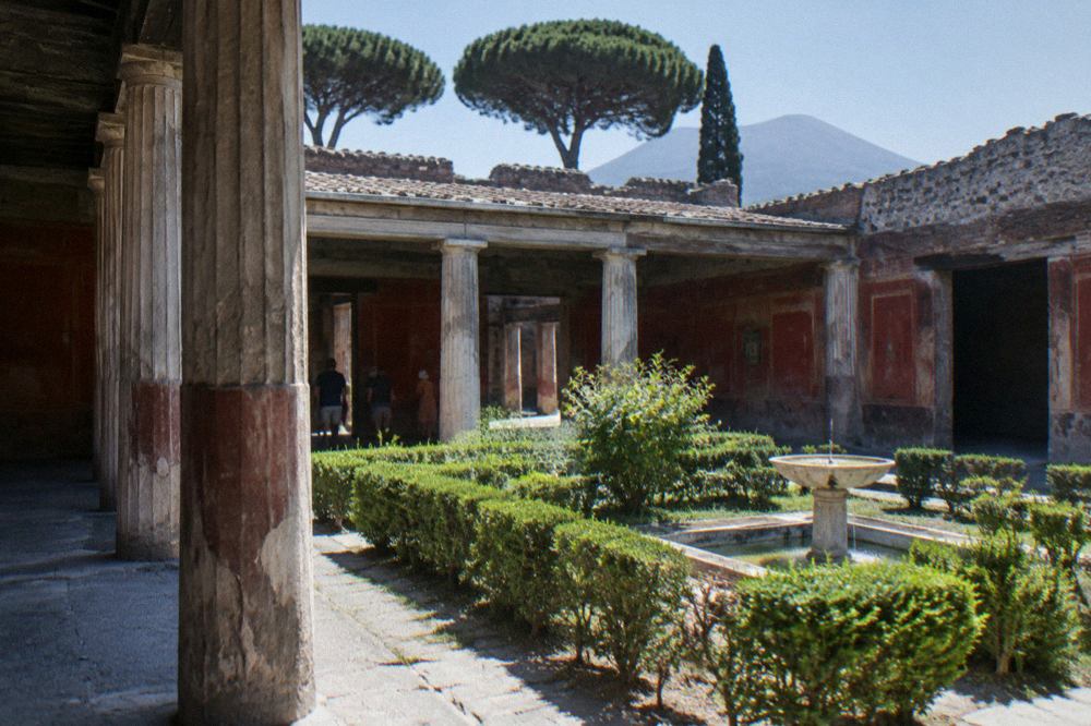 Wide view across the excavated ruins of Pompeii with stone walls, columns and Vesuvius on the horizon