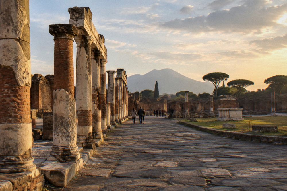 Excavated Roman forum columns with Mount Vesuvius rising in the background under a wide sky