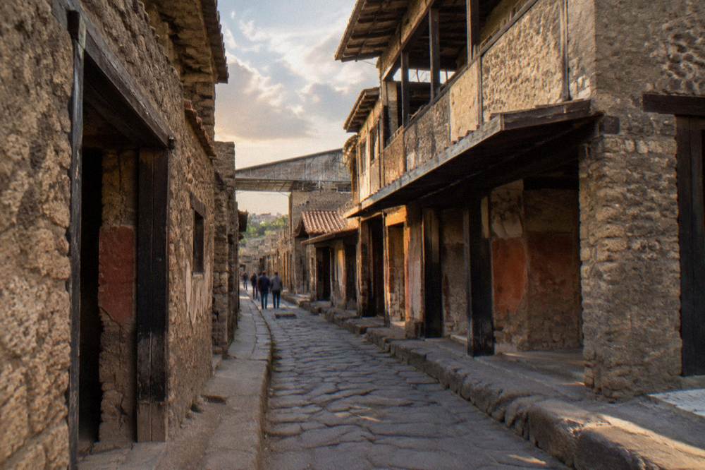 Stone-paved Roman street with wheel-worn ruts and ruined walls under a clear sky
