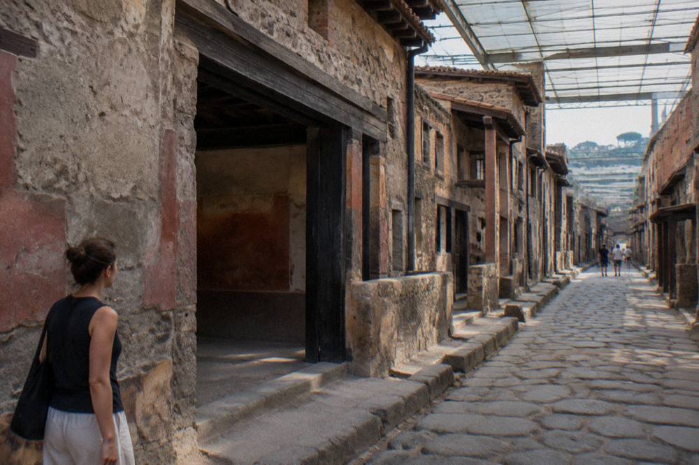 Wooden balcony overlooking excavated Roman walls and arched boat sheds by a shoreline