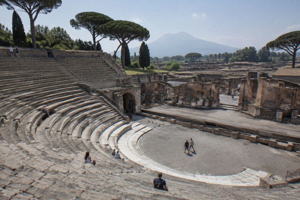 A wide stone street in Pompeii lined with ancient walls and stepping stones crossing the roadway