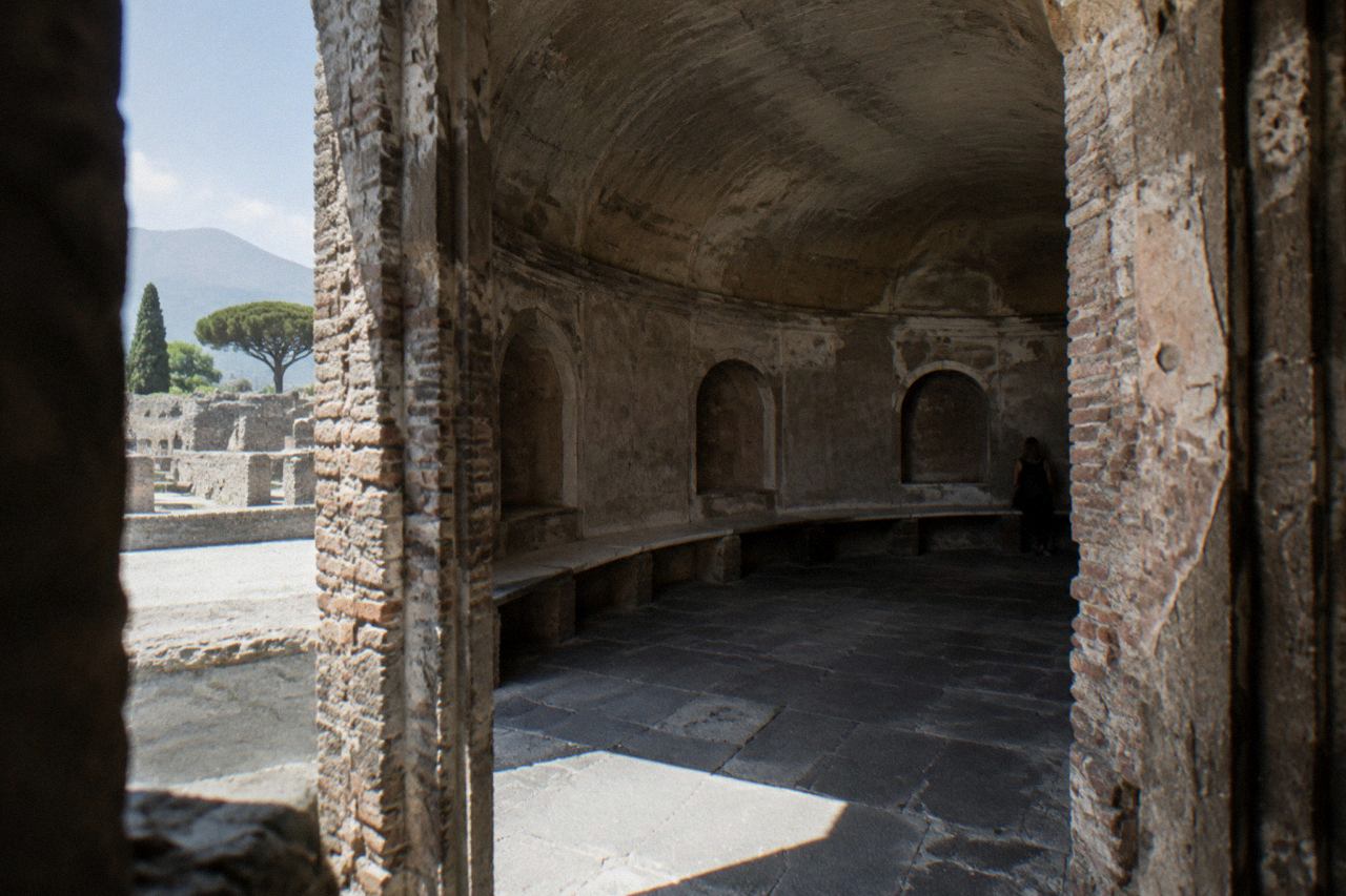 Stone-paved Roman street with ancient walls and Mount Vesuvius in the distance