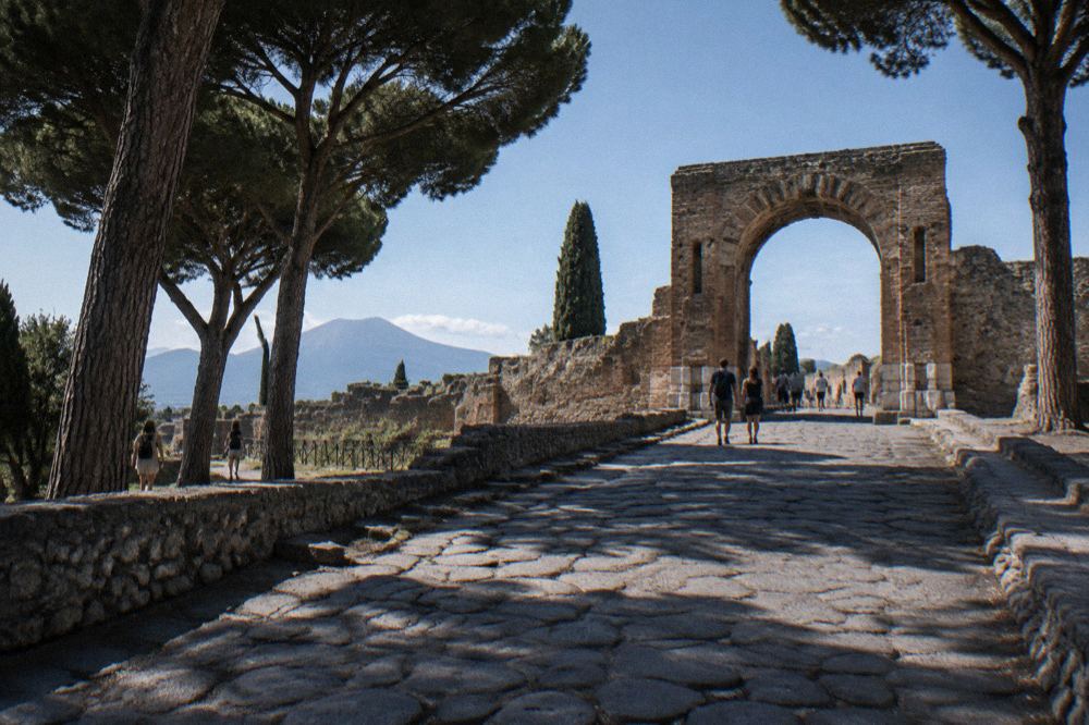 Wide stone street in Pompeii lined with low ruined walls and wheel-worn paving