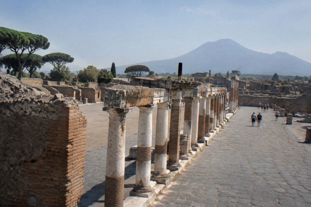 Crowded ancient Pompeian street with visitors walking between high stone walls at midday