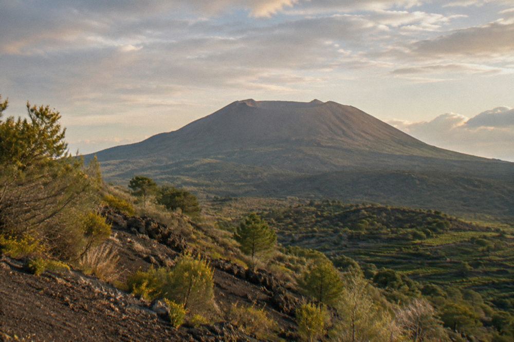 Rocky crater rim path on Mount Vesuvius with steam rising from the caldera floor