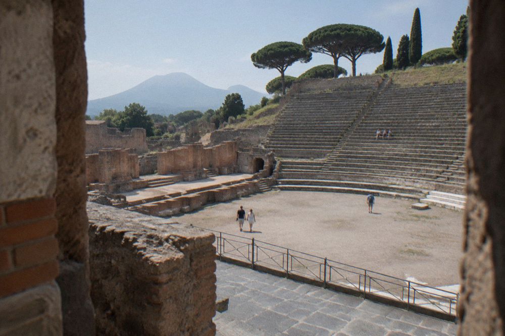 Wide uneven stone-paved street in Pompeii under strong midday sun with little shade